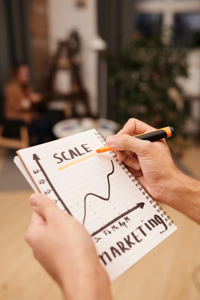 pexels photo 6476806 6476806 A person draws a marketing scale graph on a notebook with a marker.